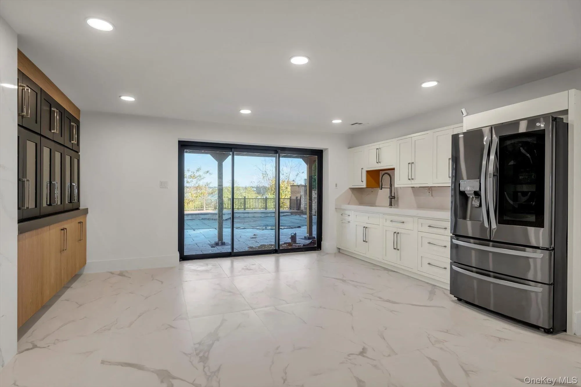 Kitchen featuring stainless steel fridge, light marble finish flooring, recessed lighting, white cabinetry, and light stone counters Kitchen featuring stainless steel fridge, light marble finish flooring, recessed lighting, white cabinetry, and light stone counters