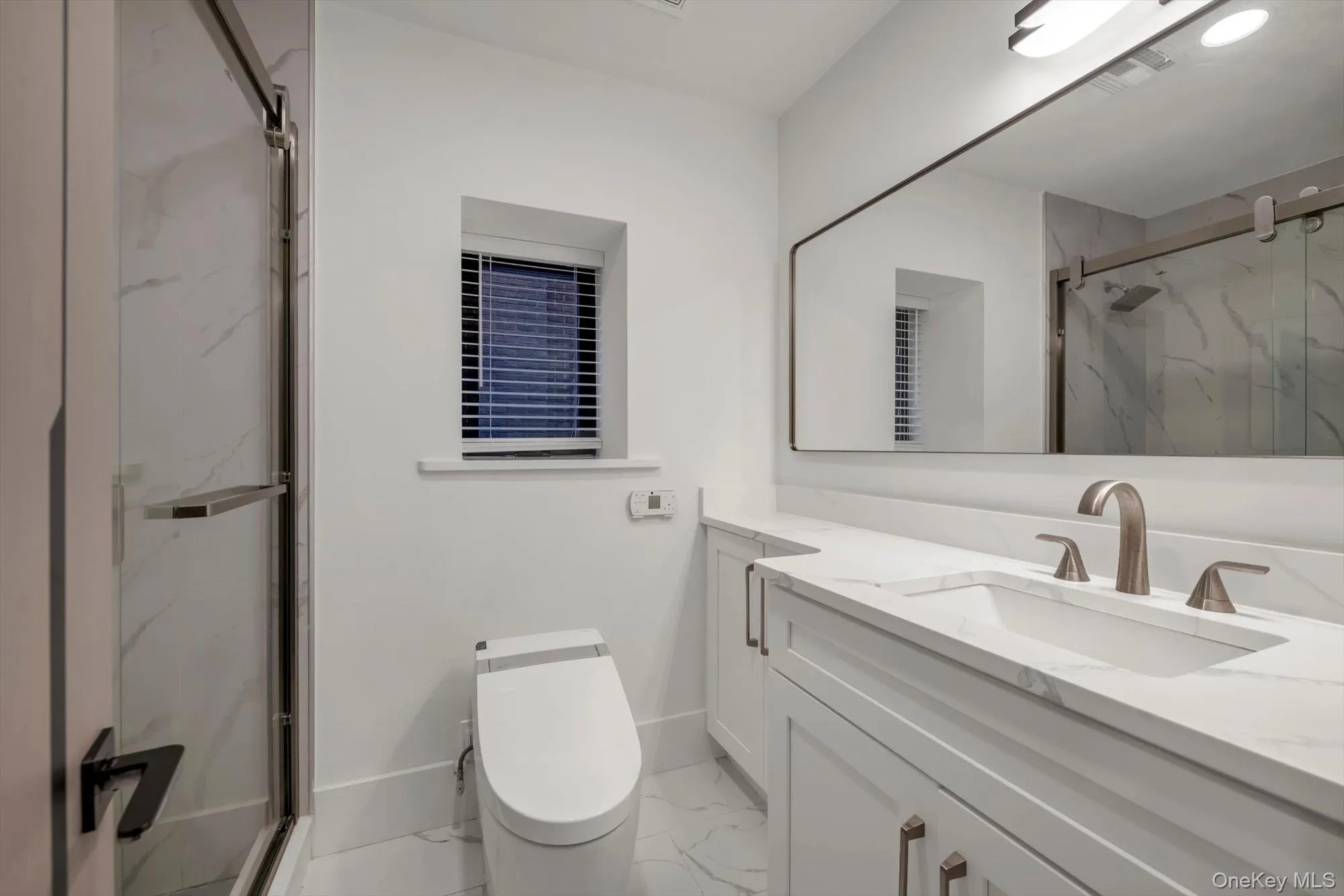 Full bathroom with a marble finish shower, vanity, and light marble finish floors Full bathroom with a marble finish shower, vanity, and light marble finish floors