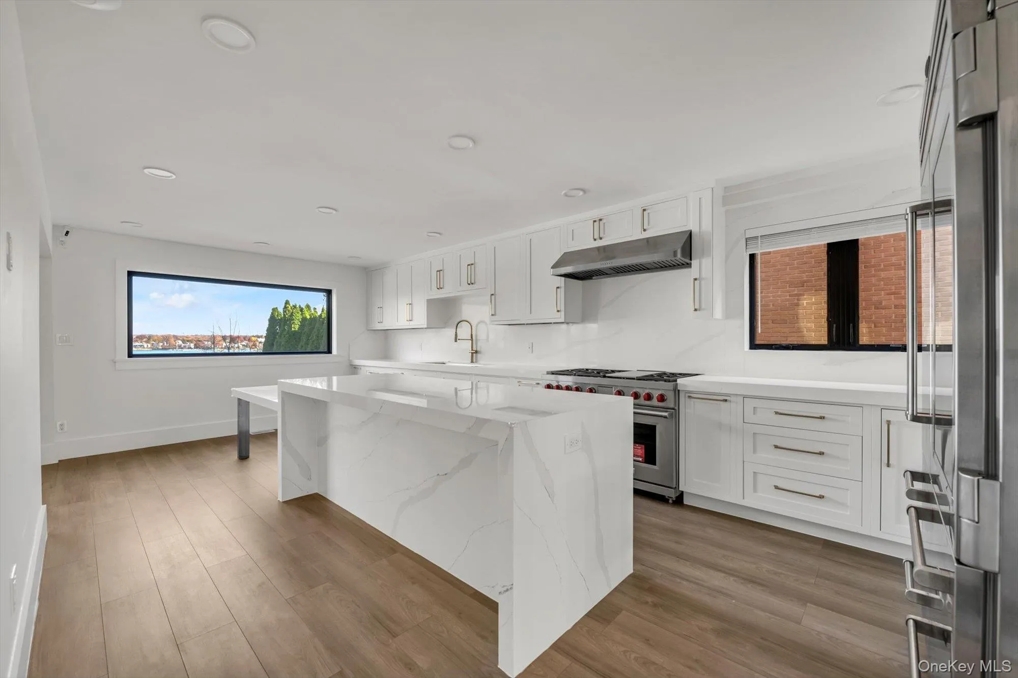 Kitchen featuring white cabinetry, light stone counters, high end appliances, a center island, and recessed lighting Kitchen featuring white cabinetry, light stone counters, high end appliances, a center island, and recessed lighting