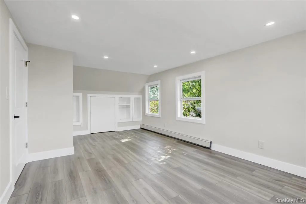 Empty room with light wood-type flooring, a baseboard heating unit, recessed lighting, and vaulted ceiling Empty room with light wood-type flooring, a baseboard heating unit, recessed lighting, and vaulted ceiling