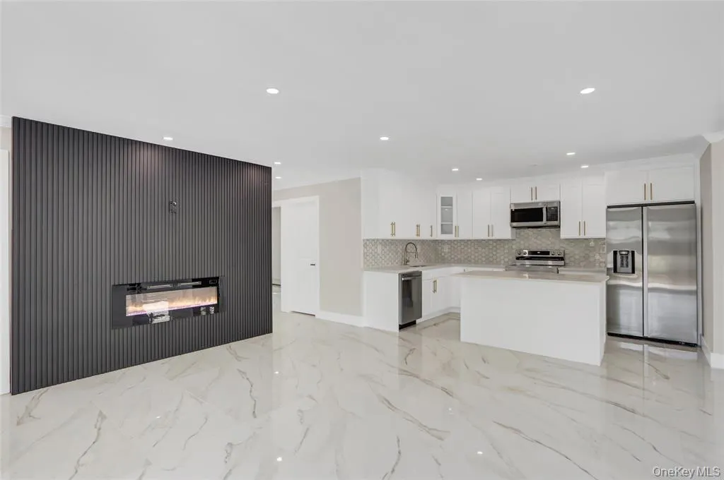 Kitchen featuring stainless steel appliances, white cabinets, a glass covered fireplace, a kitchen island, and light marble finish flooring Kitchen featuring stainless steel appliances, white cabinets, a glass covered fireplace, a kitchen island, and light marble finish flooring