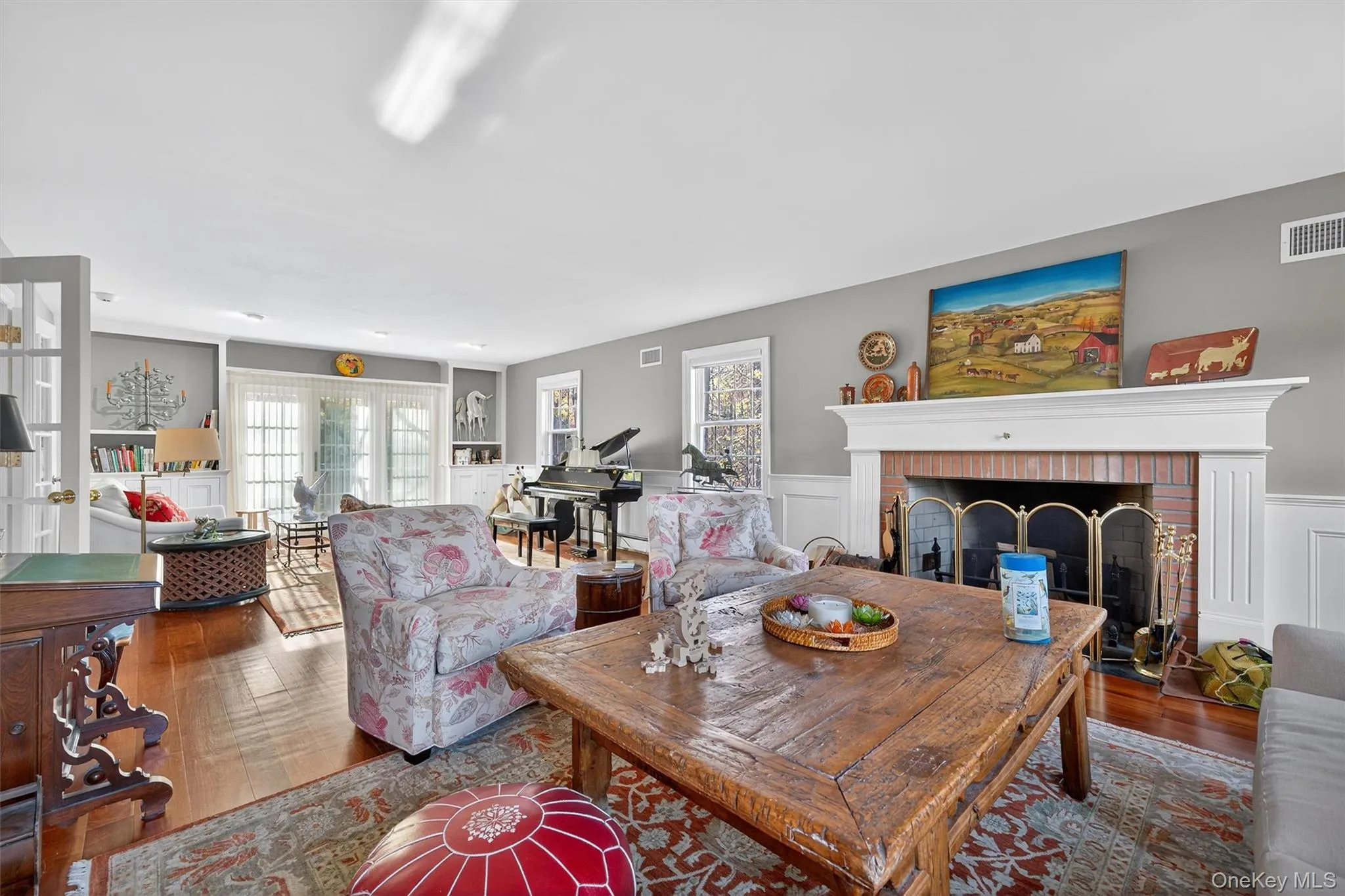 Living room with dark wood-style floors, plenty of natural light, a brick fireplace, a wainscoted wall, and a decorative wall Living room with dark wood-style floors, plenty of natural light, a brick fireplace, a wainscoted wall, and a decorative wall