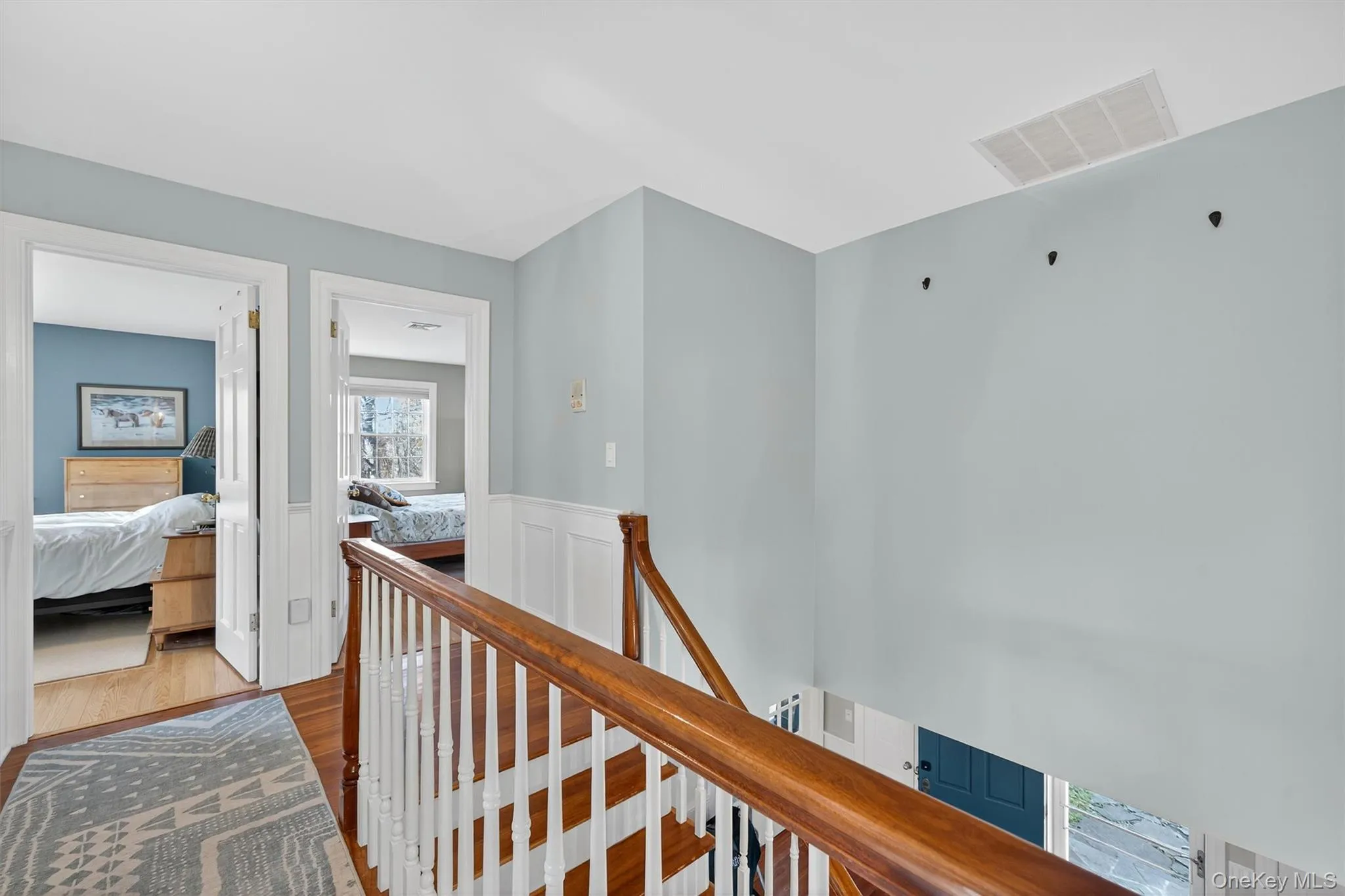 Hallway featuring an upstairs landing, wood finished floors, and wainscoting Hallway featuring an upstairs landing, wood finished floors, and wainscoting