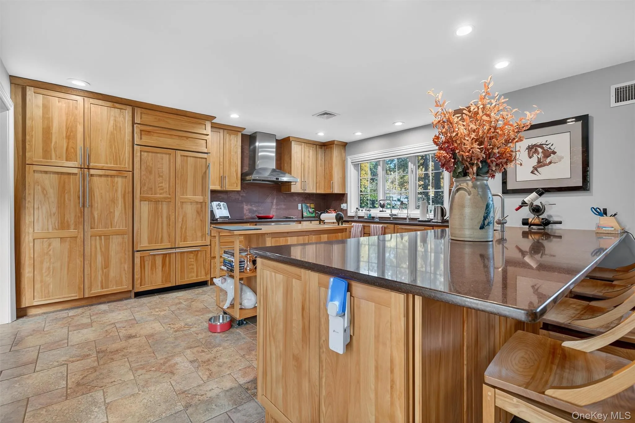 Kitchen featuring a kitchen breakfast bar, paneled fridge, backsplash, stone tile floors, and wall chimney exhaust hood Kitchen featuring a kitchen breakfast bar, paneled fridge, backsplash, stone tile floors, and wall chimney exhaust hood