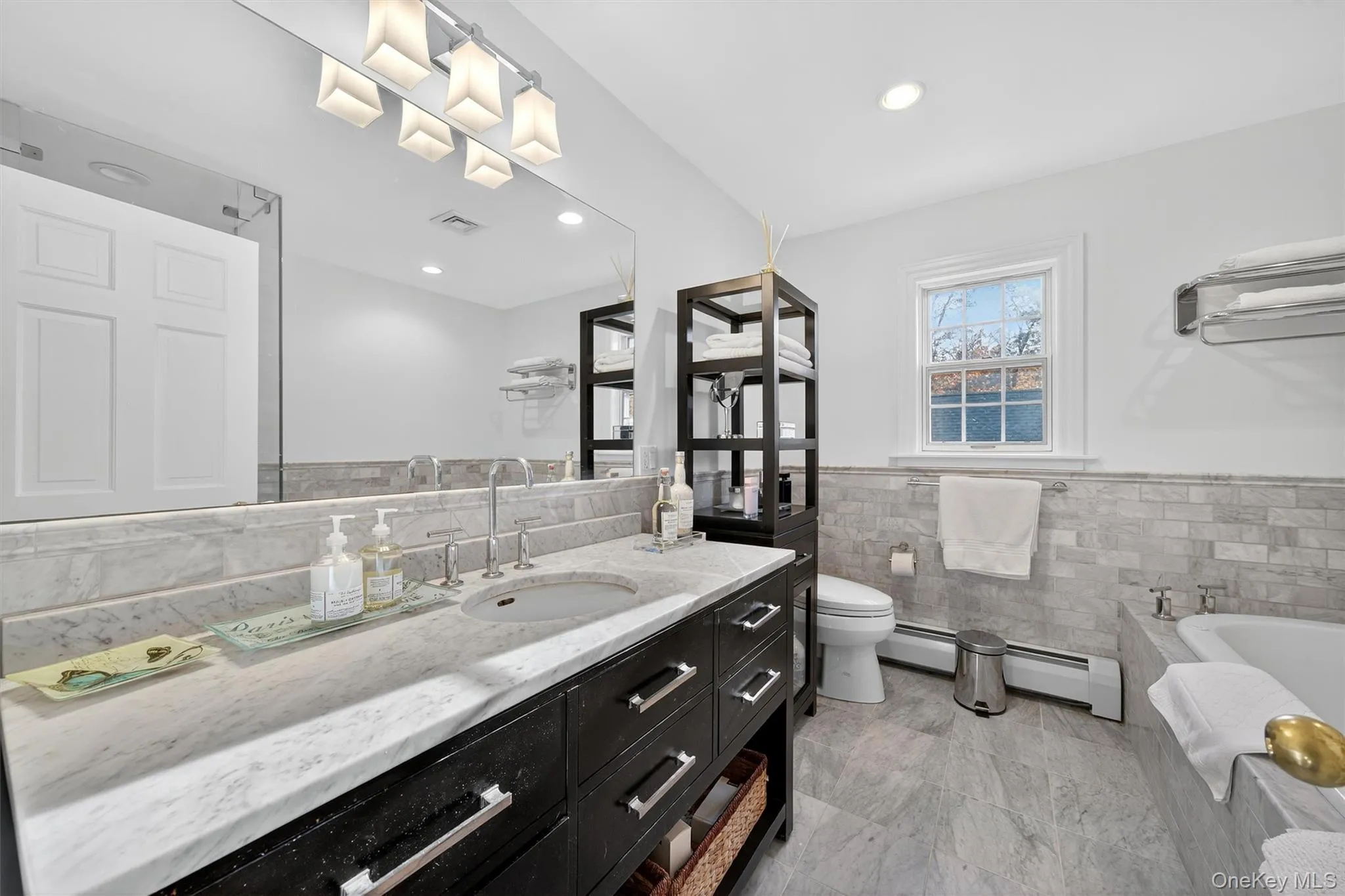 Bathroom featuring a bath, wainscoting, tile walls, vanity, and a baseboard radiator Bathroom featuring a bath, wainscoting, tile walls, vanity, and a baseboard radiator