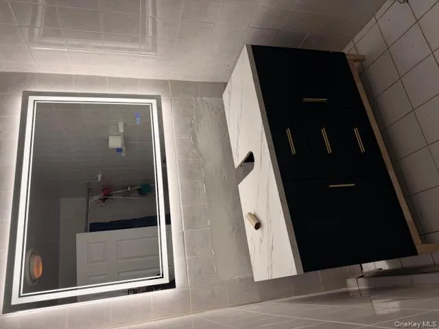 Bathroom with tile walls, vanity, light tile patterned flooring, and a shower with shower curtain Bathroom with tile walls, vanity, light tile patterned flooring, and a shower with shower curtain