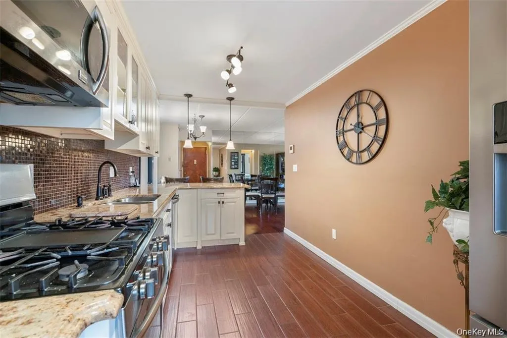 Kitchen featuring appliances with stainless steel finishes, light stone countertops, decorative light fixtures, dark wood-style floors, and white cabinets Kitchen featuring appliances with stainless steel finishes, light stone countertops, decorative light fixtures, dark wood-style floors, and white cabinets