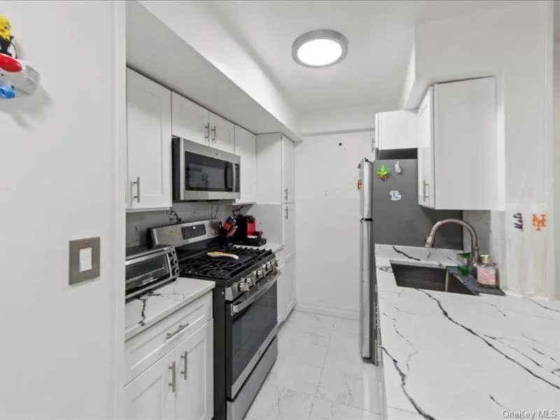 Kitchen featuring stainless steel appliances, light stone counters, white cabinets, and light marble finish floors Kitchen featuring stainless steel appliances, light stone counters, white cabinets, and light marble finish floors