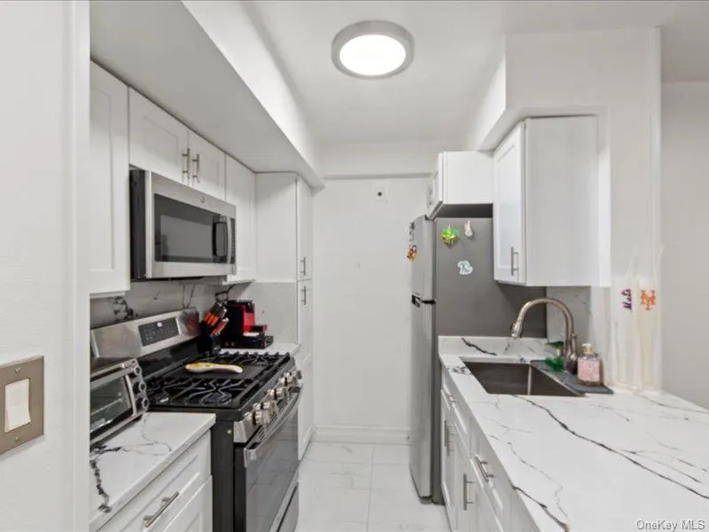 Kitchen with stainless steel appliances, light stone counters, white cabinets, and light marble finish floors Kitchen with stainless steel appliances, light stone counters, white cabinets, and light marble finish floors