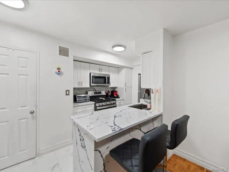 Kitchen featuring light stone counters, white cabinets, a breakfast bar area, stainless steel appliances, and a peninsula Kitchen featuring light stone counters, white cabinets, a breakfast bar area, stainless steel appliances, and a peninsula
