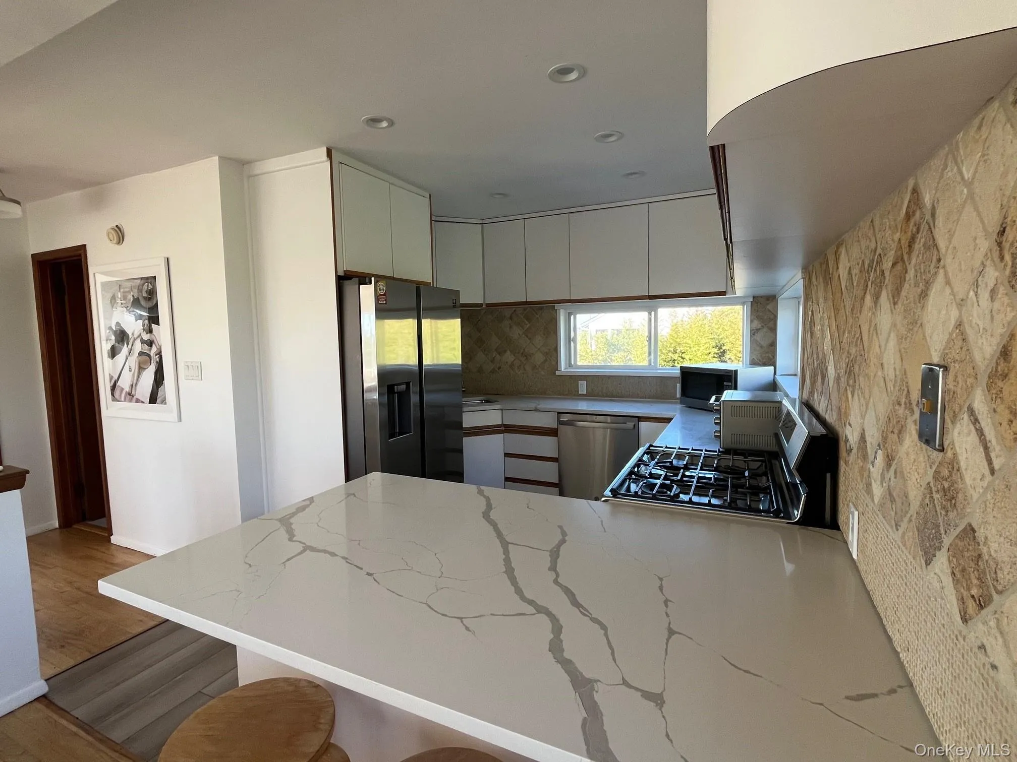 Kitchen with white cabinets, appliances with stainless steel finishes, a peninsula, light wood-style floors, and light stone countertops Kitchen with white cabinets, appliances with stainless steel finishes, a peninsula, light wood-style floors, and light stone countertops