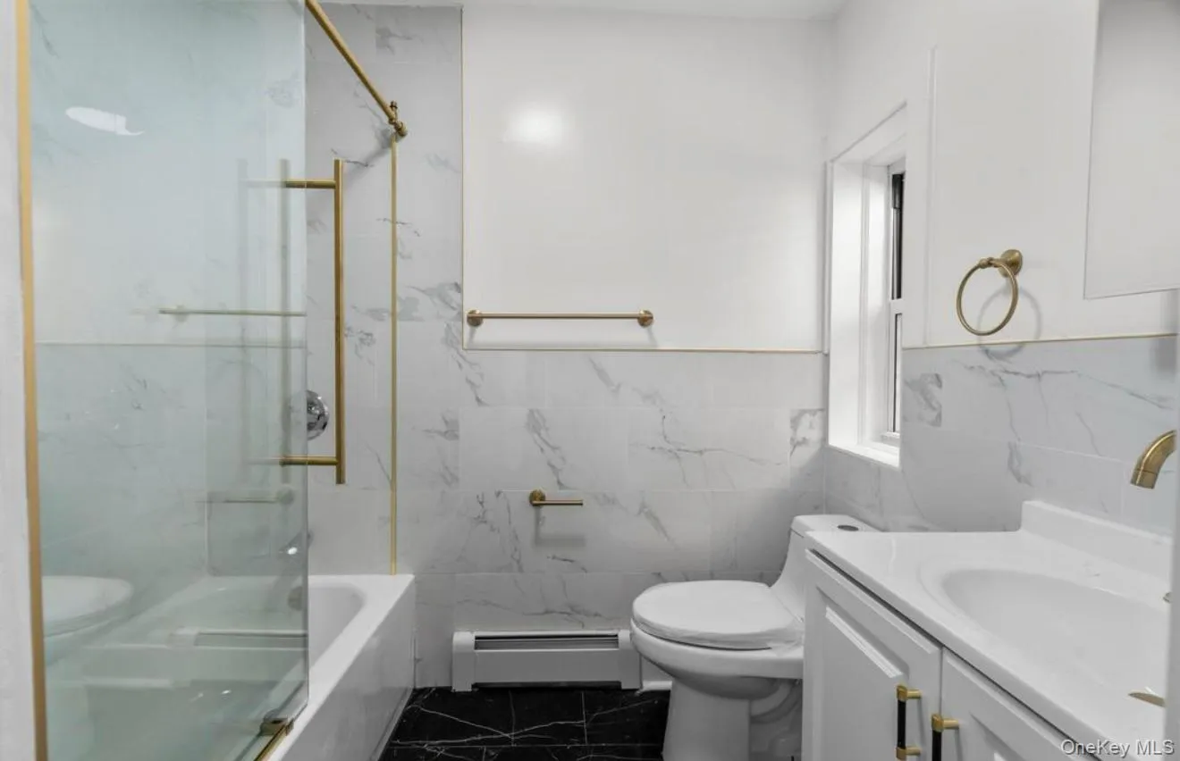 Full bath featuring vanity, tile walls, dark marble finish floors, baseboard heating, and a combined bath / shower with marble appearance Full bath featuring vanity, tile walls, dark marble finish floors, baseboard heating, and a combined bath / shower with marble appearance