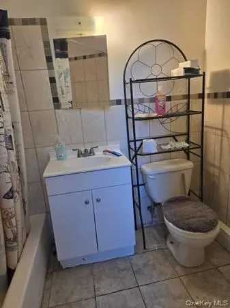 Bathroom featuring tile walls, vanity, light tile patterned flooring, wainscoting, and shower / bathtub combination with curtain Bathroom featuring tile walls, vanity, light tile patterned flooring, wainscoting, and shower / bathtub combination with curtain
