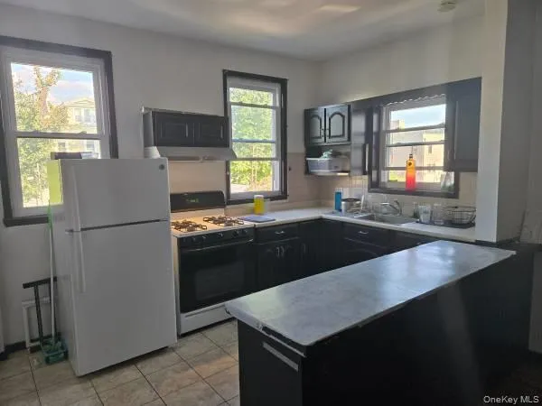 Kitchen featuring range with gas cooktop, freestanding refrigerator, light tile patterned floors, and light countertops Kitchen featuring range with gas cooktop, freestanding refrigerator, light tile patterned floors, and light countertops