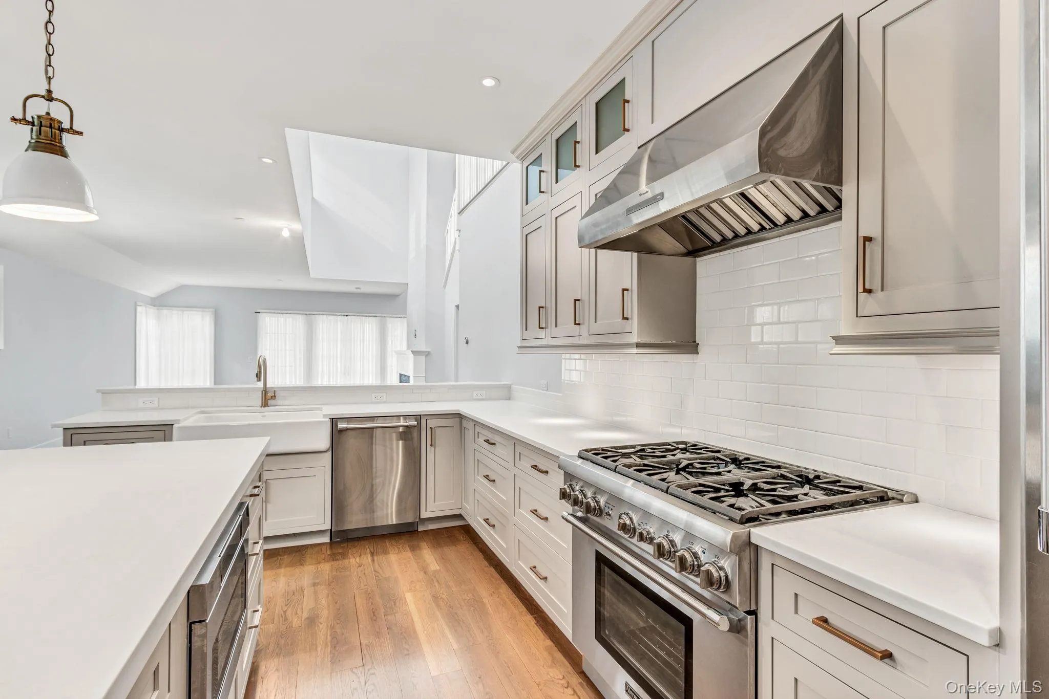 Kitchen featuring stainless steel appliances, ventilation hood, glass insert cabinets, hanging light fixtures, and light wood-style floors Kitchen featuring stainless steel appliances, ventilation hood, glass insert cabinets, hanging light fixtures, and light wood-style floors