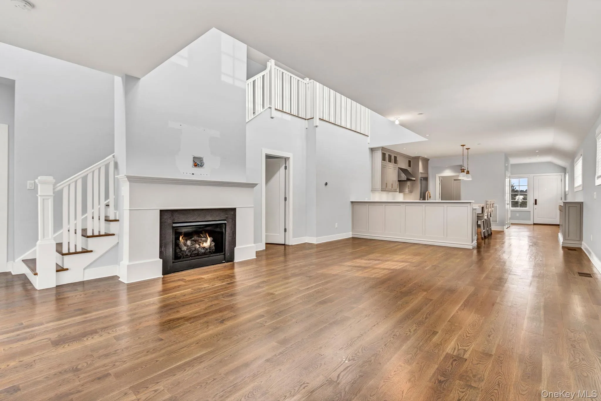 Unfurnished living room featuring a lit fireplace, light wood-type flooring, stairway, and lofted ceiling Unfurnished living room featuring a lit fireplace, light wood-type flooring, stairway, and lofted ceiling