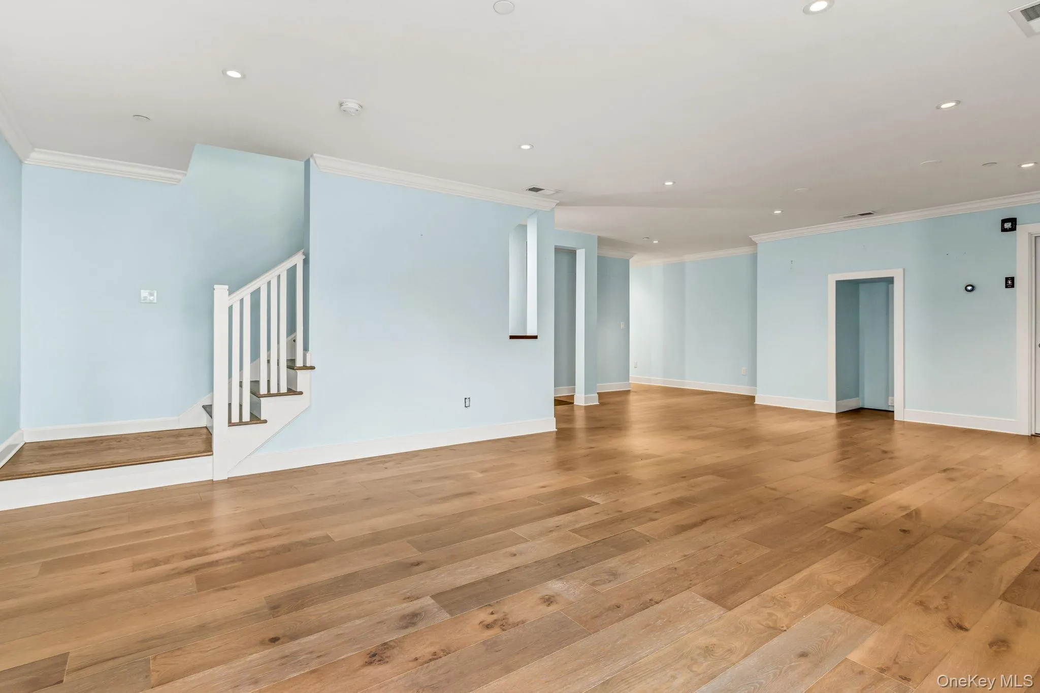 Unfurnished living room with ornamental molding, stairway, light wood finished floors, and recessed lighting Unfurnished living room with ornamental molding, stairway, light wood finished floors, and recessed lighting
