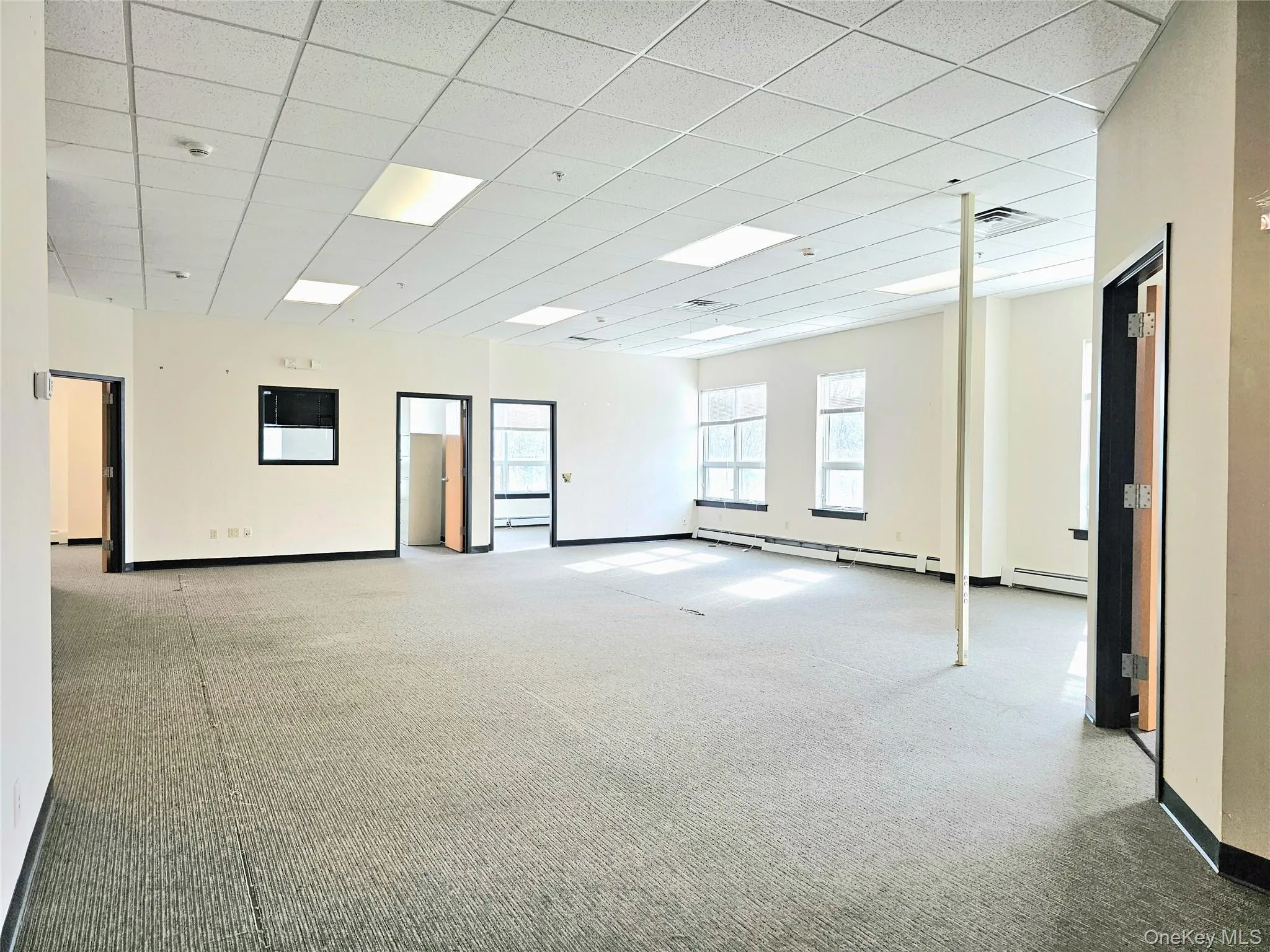 Empty room with light colored carpet, a paneled ceiling, and baseboard heating Empty room with light colored carpet, a paneled ceiling, and baseboard heating