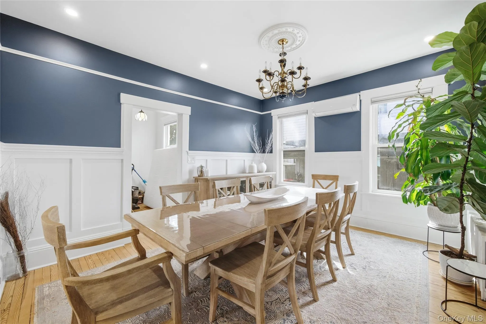 Dining area featuring light wood-style floors, a decorative wall, a chandelier, a wainscoted wall, and a wall mounted AC Dining area featuring light wood-style floors, a decorative wall, a chandelier, a wainscoted wall, and a wall mounted AC