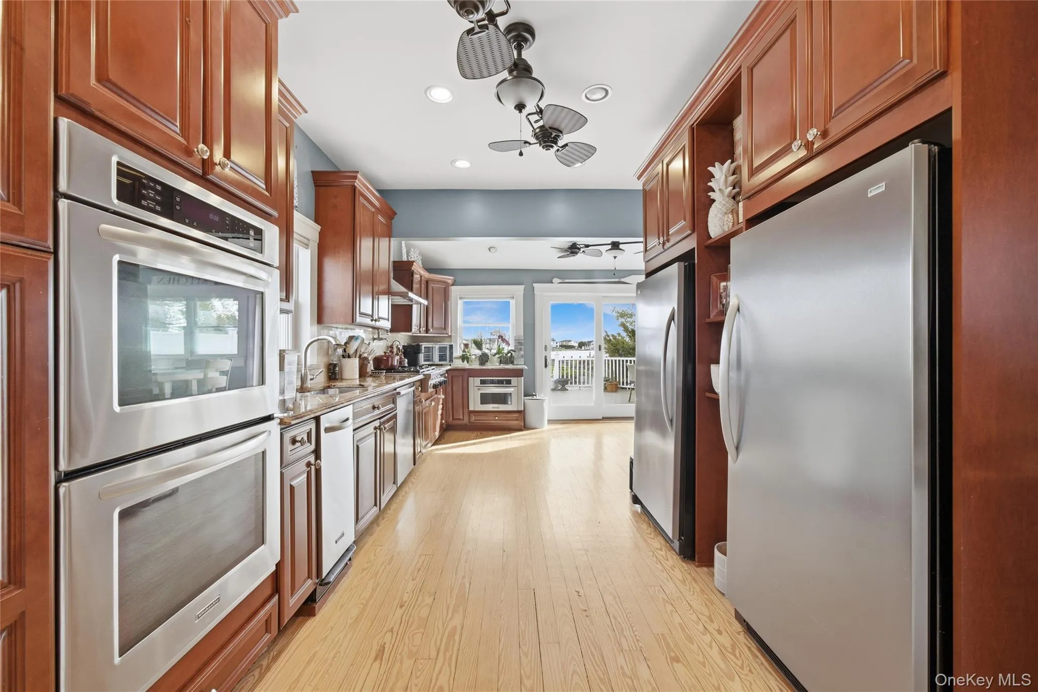 Kitchen with stainless steel appliances, a ceiling fan, light stone countertops, brown cabinets, and light wood-type flooring Kitchen with stainless steel appliances, a ceiling fan, light stone countertops, brown cabinets, and light wood-type flooring