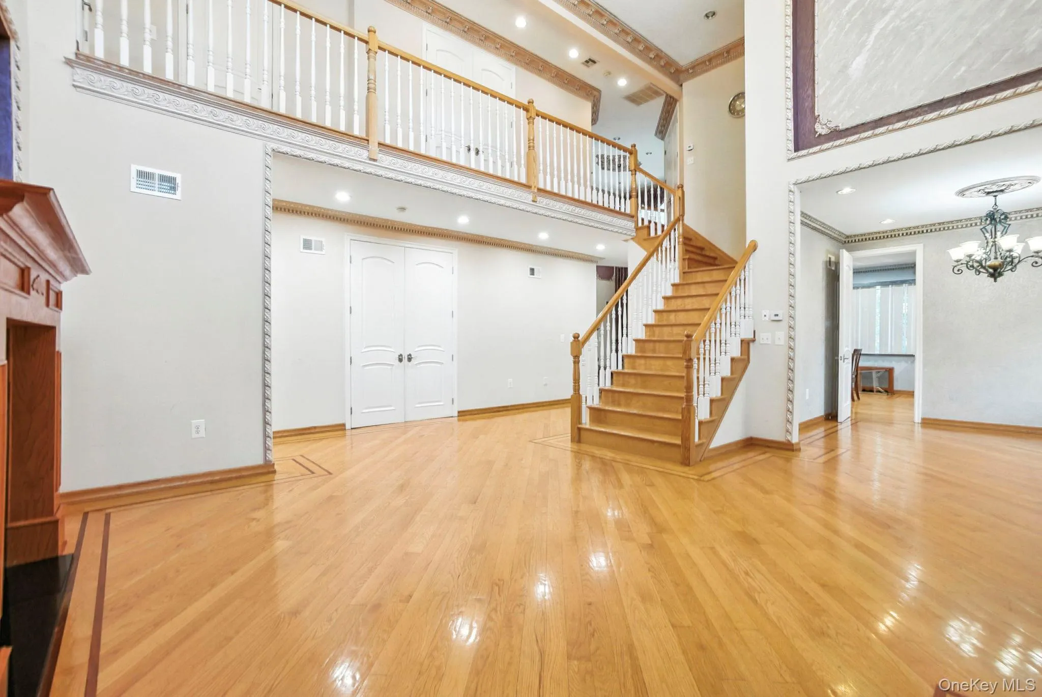 Unfurnished living room with a towering ceiling, light wood finished floors, stairway, ornamental molding, and a chandelier Unfurnished living room with a towering ceiling, light wood finished floors, stairway, ornamental molding, and a chandelier