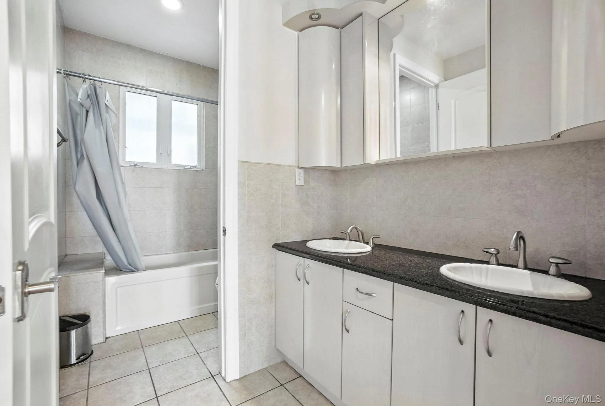 Bathroom with shower / tub combo with curtain, double vanity, light tile patterned floors, and tile walls Bathroom with shower / tub combo with curtain, double vanity, light tile patterned floors, and tile walls