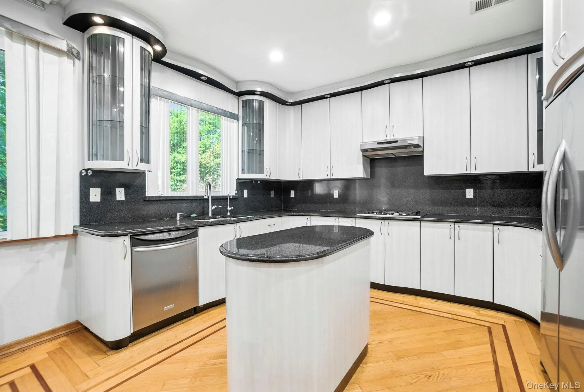 Kitchen with tasteful backsplash, dark stone counters, a center island, glass insert cabinets, and stainless steel appliances Kitchen with tasteful backsplash, dark stone counters, a center island, glass insert cabinets, and stainless steel appliances