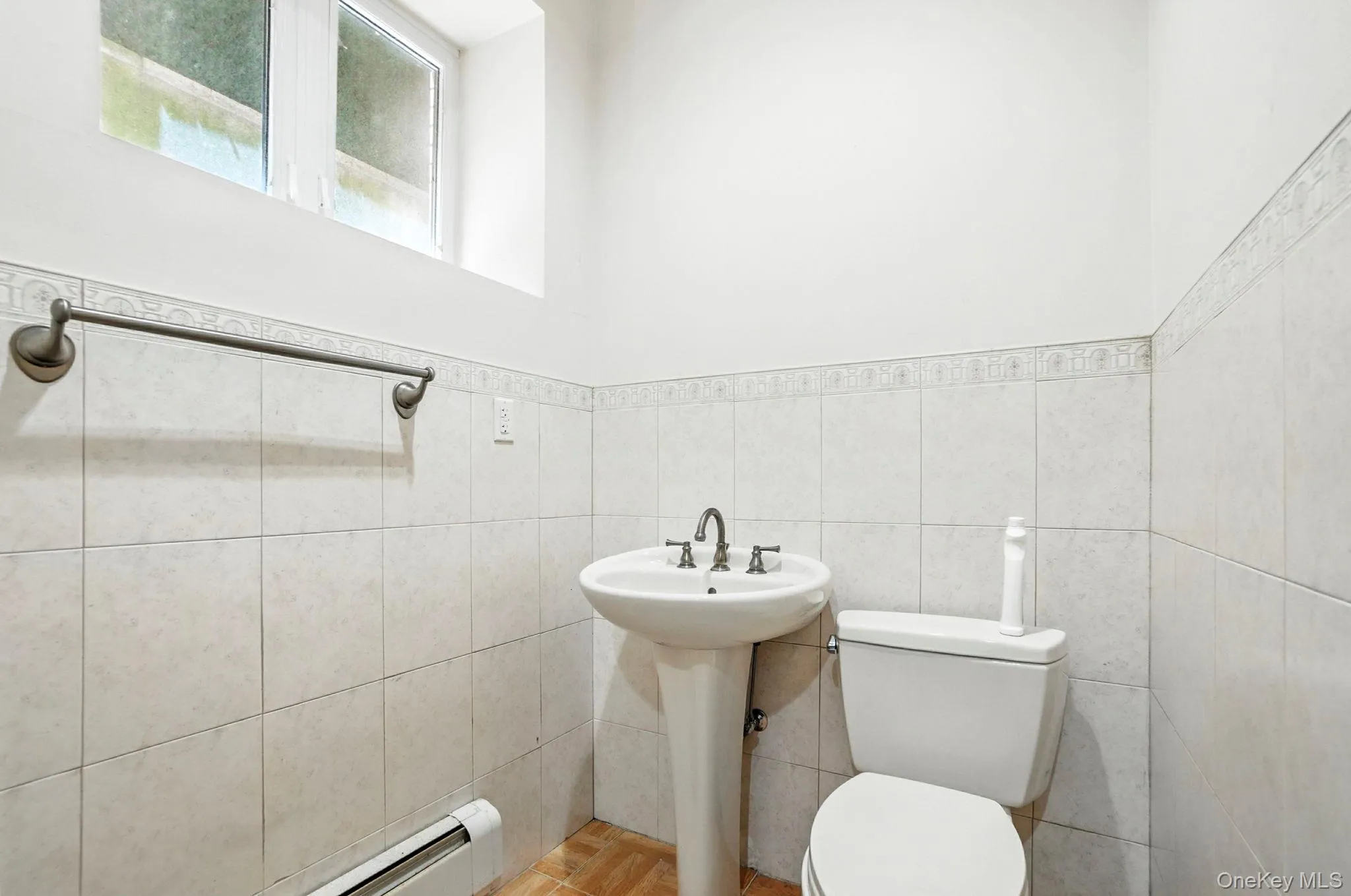 Half bath with baseboard heating, a wainscoted wall, and tile walls Half bath with baseboard heating, a wainscoted wall, and tile walls