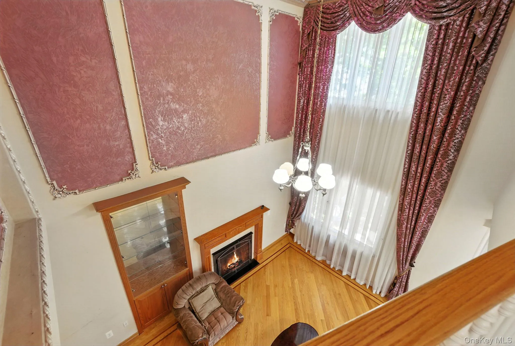 Living room with a warm lit fireplace, wood finished floors, and a chandelier Living room with a warm lit fireplace, wood finished floors, and a chandelier