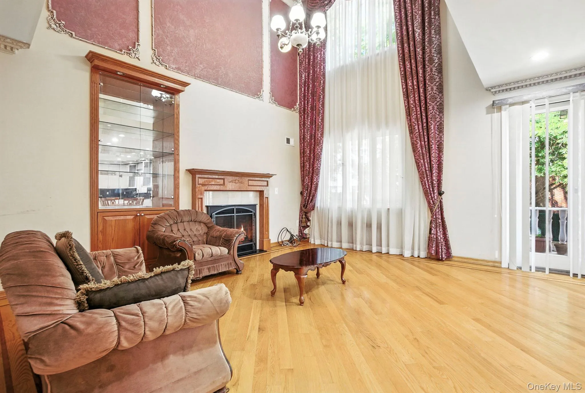 Sitting room featuring a fireplace with flush hearth, a towering ceiling, light wood-type flooring, and a chandelier Sitting room featuring a fireplace with flush hearth, a towering ceiling, light wood-type flooring, and a chandelier