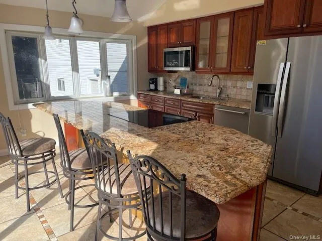 Kitchen with appliances with stainless steel finishes, light tile patterned floors, pendant lighting, sink, and tasteful backsplash Kitchen with appliances with stainless steel finishes, light tile patterned floors, pendant lighting, sink, and tasteful backsplash