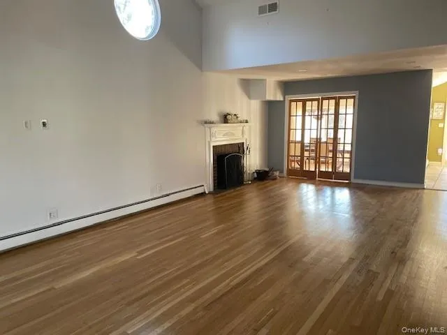 Unfurnished living room with a towering ceiling, dark hardwood / wood-style floors, a baseboard radiator, and a fireplace Unfurnished living room with a towering ceiling, dark hardwood / wood-style floors, a baseboard radiator, and a fireplace