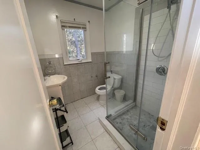 Bathroom with toilet, vanity, tile patterned floors, tile walls, and a shower with shower door Bathroom with toilet, vanity, tile patterned floors, tile walls, and a shower with shower door