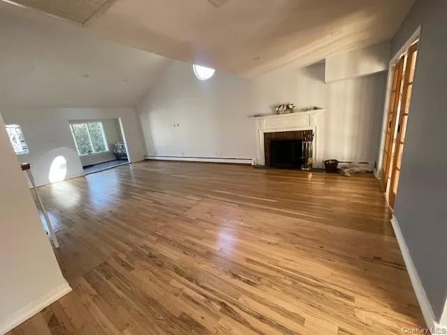 Unfurnished living room featuring a baseboard heating unit, vaulted ceiling, a fireplace, and light hardwood / wood-style floors Unfurnished living room featuring a baseboard heating unit, vaulted ceiling, a fireplace, and light hardwood / wood-style floors