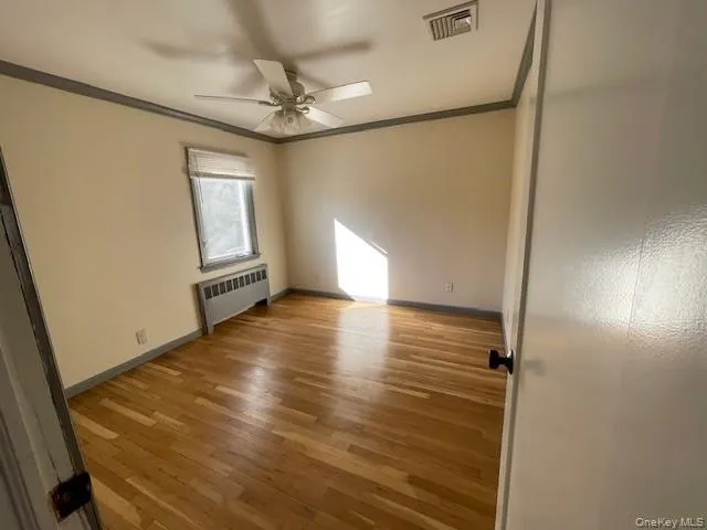 Spare room featuring radiator, ornamental molding, ceiling fan, and light hardwood / wood-style flooring Spare room featuring radiator, ornamental molding, ceiling fan, and light hardwood / wood-style flooring