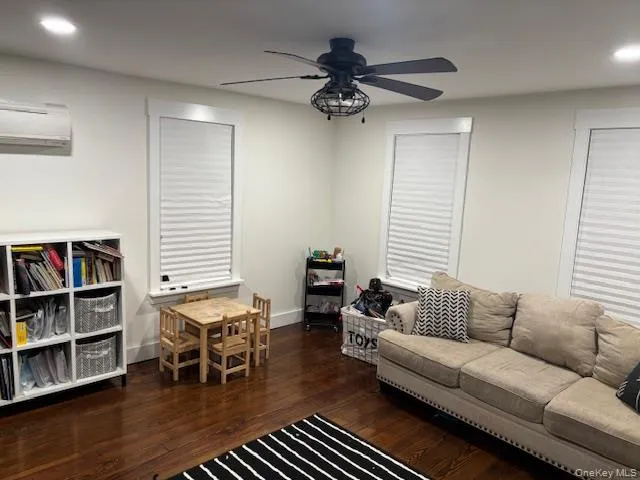 Living room featuring dark wood finished floors, recessed lighting, ceiling fan, and a wall unit AC Living room featuring dark wood finished floors, recessed lighting, ceiling fan, and a wall unit AC