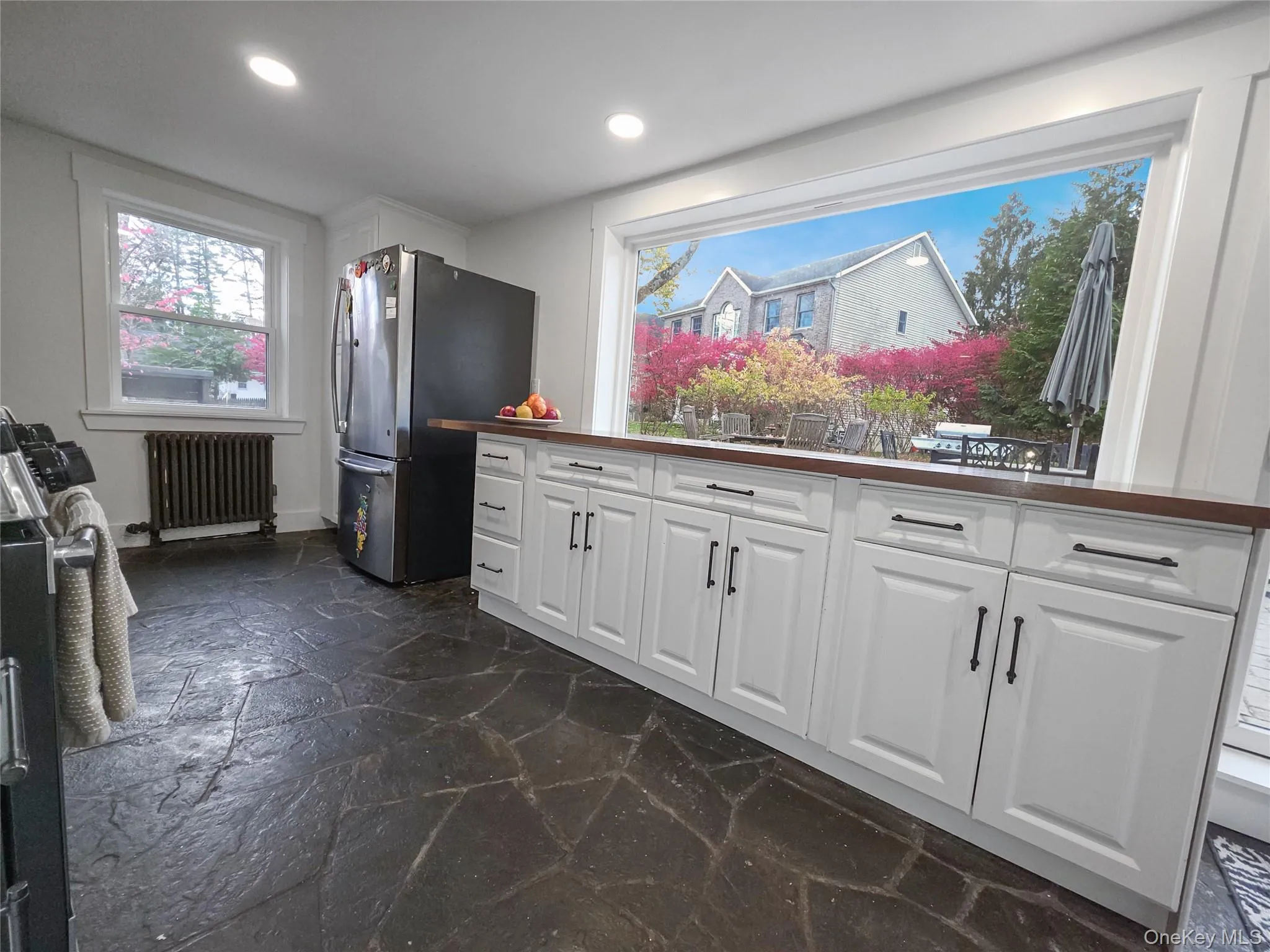 Kitchen featuring white cabinetry, stainless steel appliances, stone tile flooring, radiator, and dark countertops Kitchen featuring white cabinetry, stainless steel appliances, stone tile flooring, radiator, and dark countertops