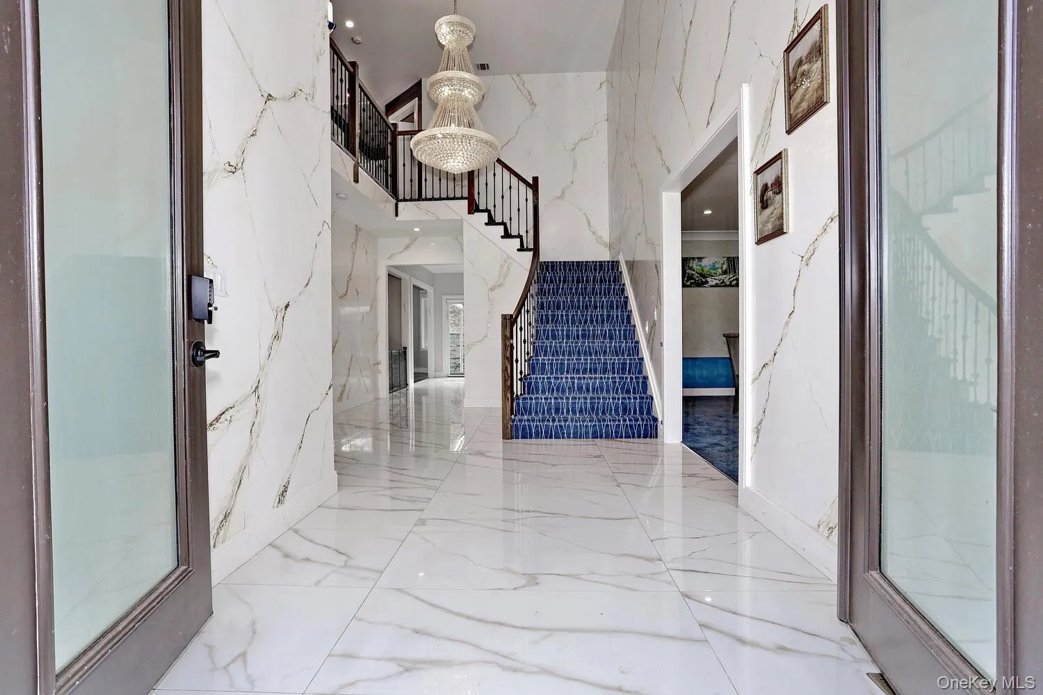 Foyer entrance with stairway, a chandelier, marble tiled flooring, a high ceiling, and stone wall Foyer entrance with stairway, a chandelier, marble tiled flooring, a high ceiling, and stone wall