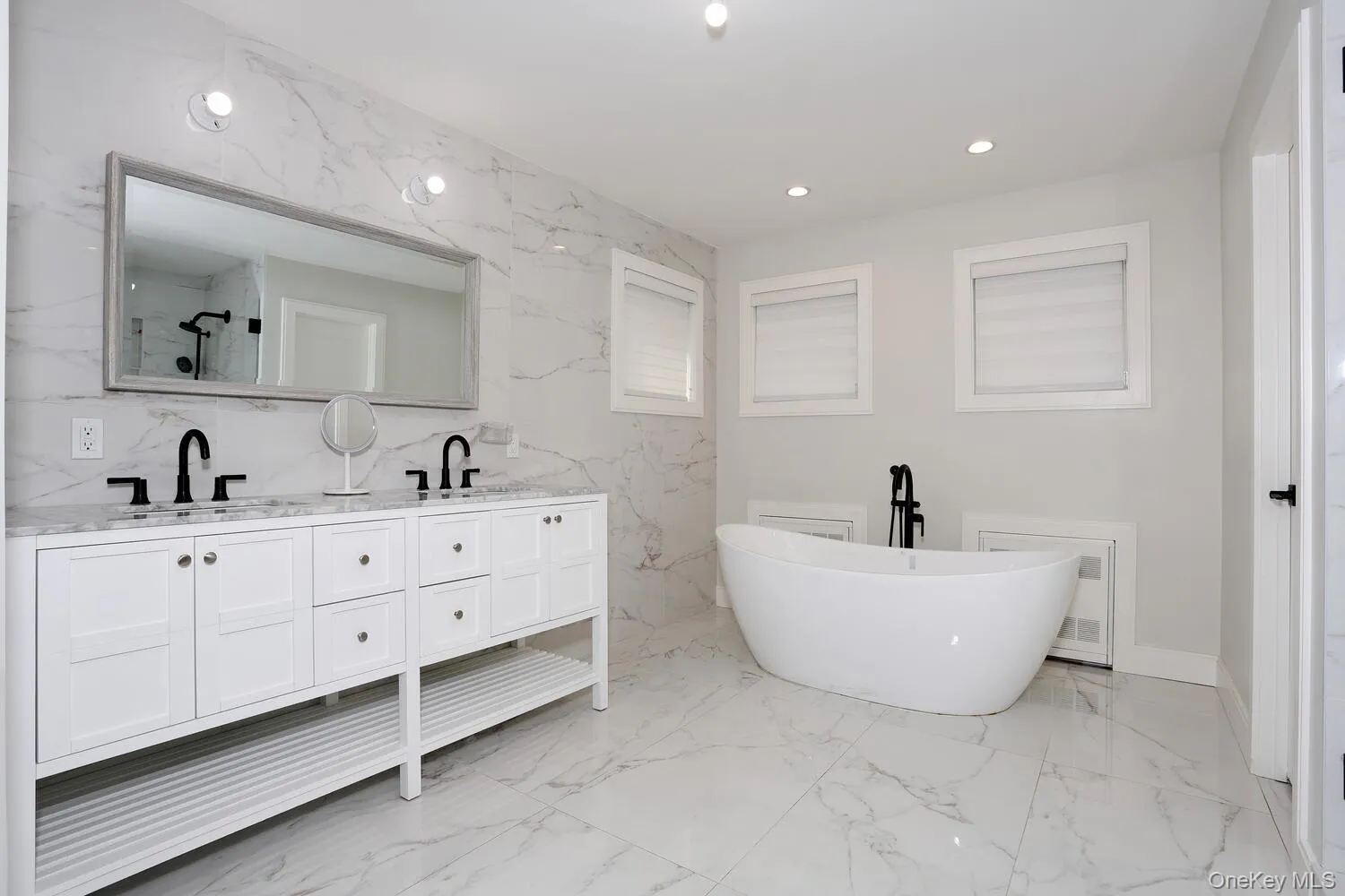 Bathroom featuring stone wall, a soaking tub, recessed lighting, double vanity, and light marble finish floors Bathroom featuring stone wall, a soaking tub, recessed lighting, double vanity, and light marble finish floors