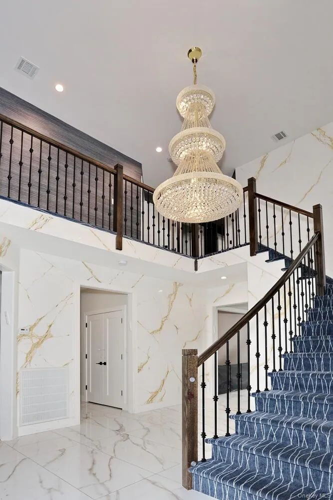 Staircase with stone wall, marble tiled floors, a high ceiling, a chandelier, and recessed lighting Staircase with stone wall, marble tiled floors, a high ceiling, a chandelier, and recessed lighting
