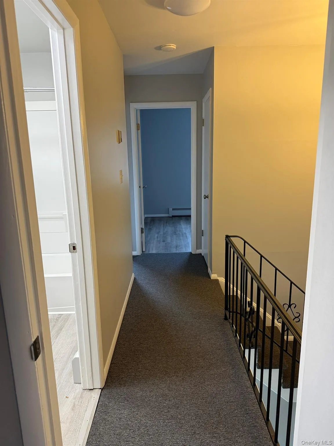 Corridor with an upstairs landing, carpet floors, and a baseboard radiator Corridor with an upstairs landing, carpet floors, and a baseboard radiator