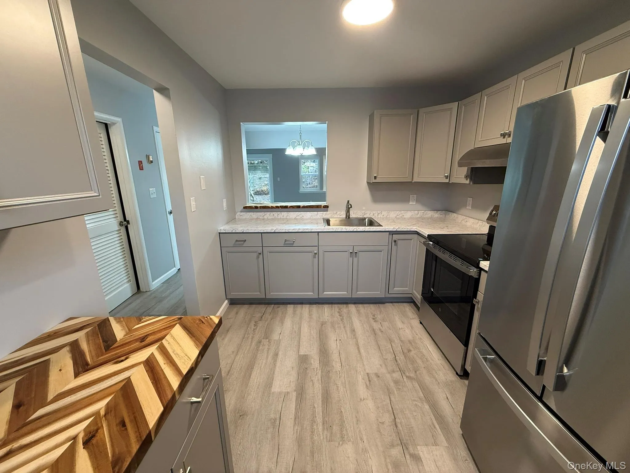 Kitchen featuring gray cabinets, stainless steel appliances, a chandelier, light wood-type flooring, and light countertops Kitchen featuring gray cabinets, stainless steel appliances, a chandelier, light wood-type flooring, and light countertops