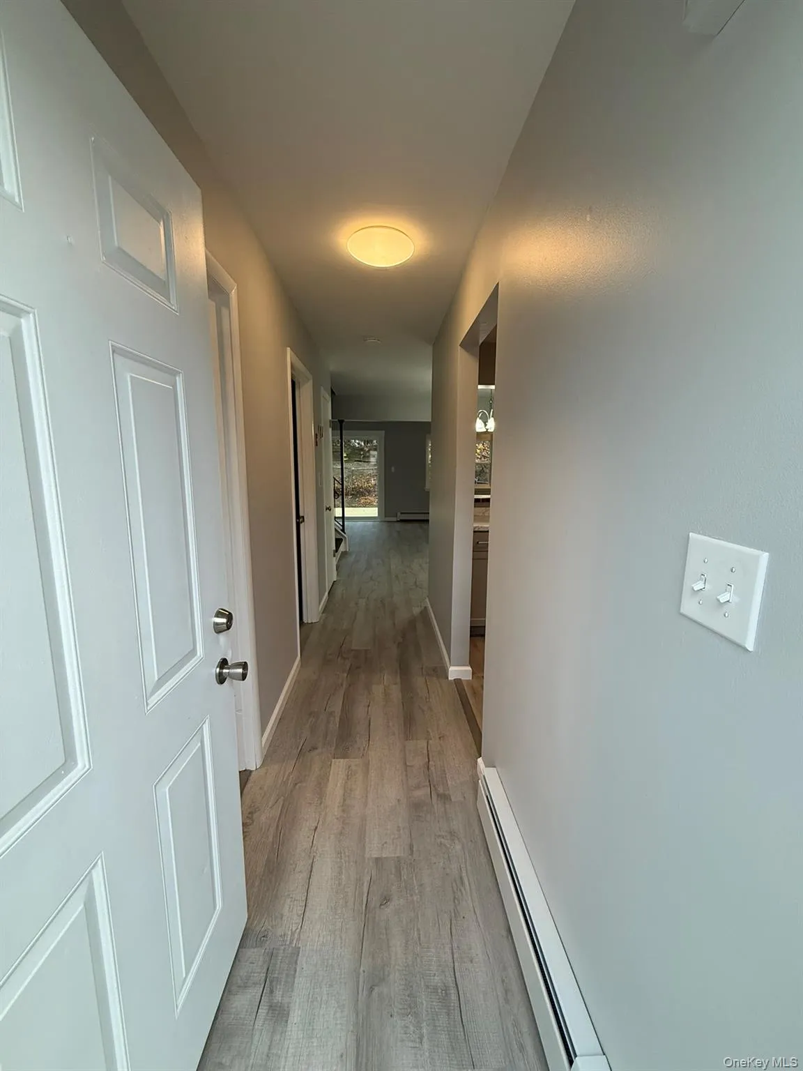 Hallway featuring a baseboard heating unit and light wood finished floors Hallway featuring a baseboard heating unit and light wood finished floors