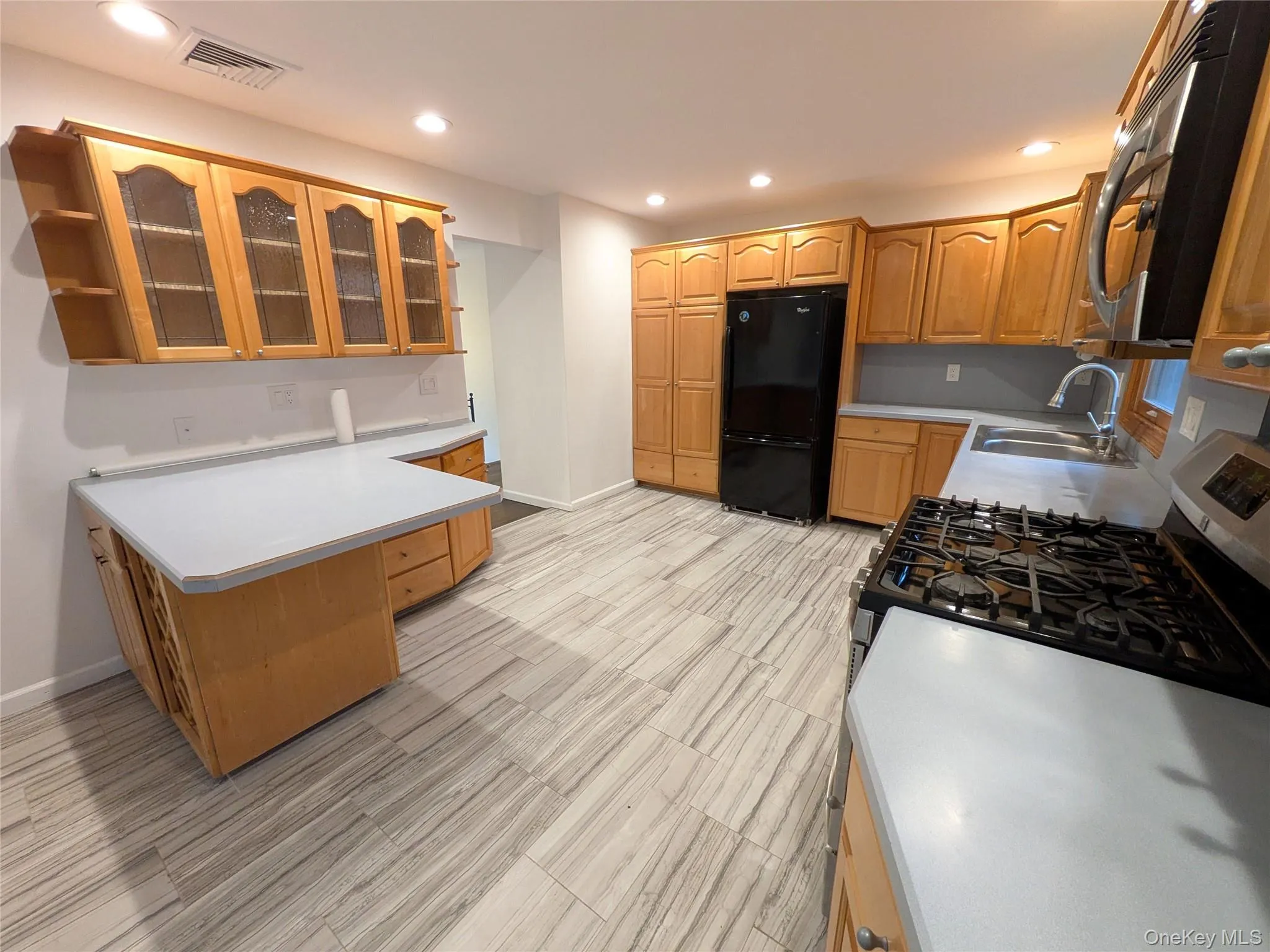 Kitchen with open shelves, glass insert cabinets, black appliances, wine storage cabinet, light countertops & back-splash, and recessed lighting. Kitchen with open shelves, glass insert cabinets, black appliances, wine storage cabinet, light countertops & back-splash, and recessed lighting.