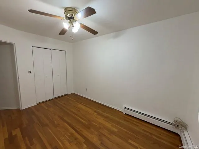 Unfurnished bedroom with dark wood-style floors, a baseboard heating unit, ceiling fan, and a closet Unfurnished bedroom with dark wood-style floors, a baseboard heating unit, ceiling fan, and a closet