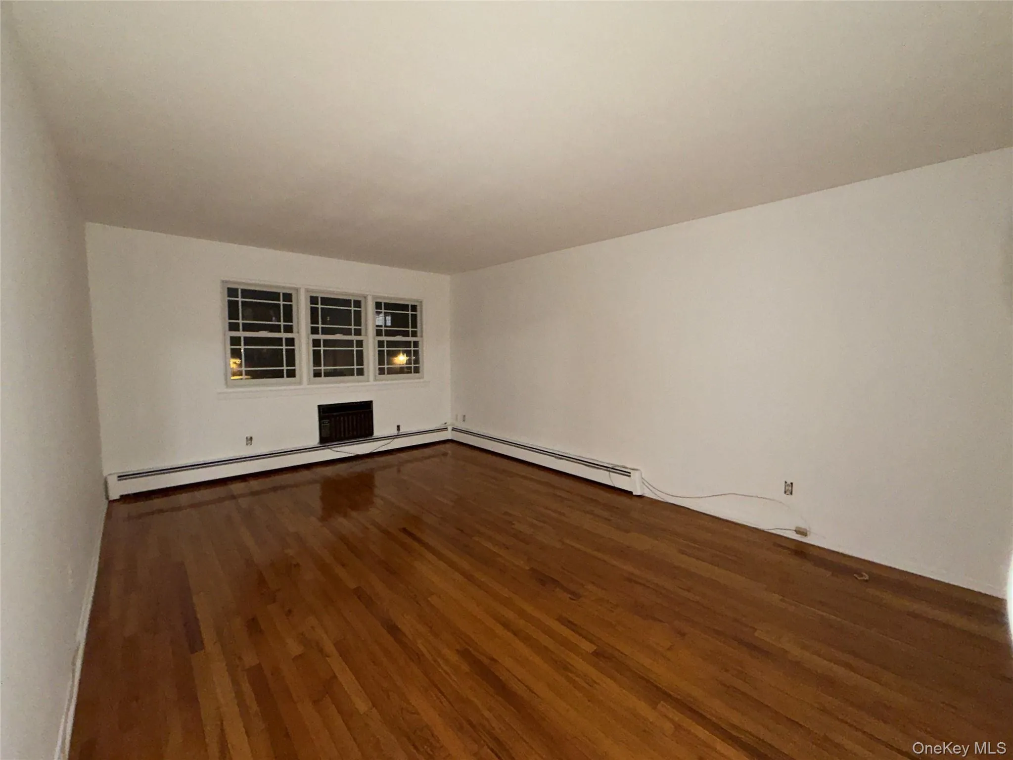 Empty room featuring dark wood finished floors and baseboard heating Empty room featuring dark wood finished floors and baseboard heating