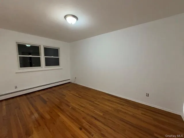 Empty room with dark wood-style floors and baseboard heating Empty room with dark wood-style floors and baseboard heating