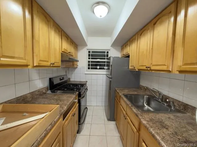 Kitchen with gas range oven, backsplash, light tile patterned floors, and under cabinet range hood Kitchen with gas range oven, backsplash, light tile patterned floors, and under cabinet range hood