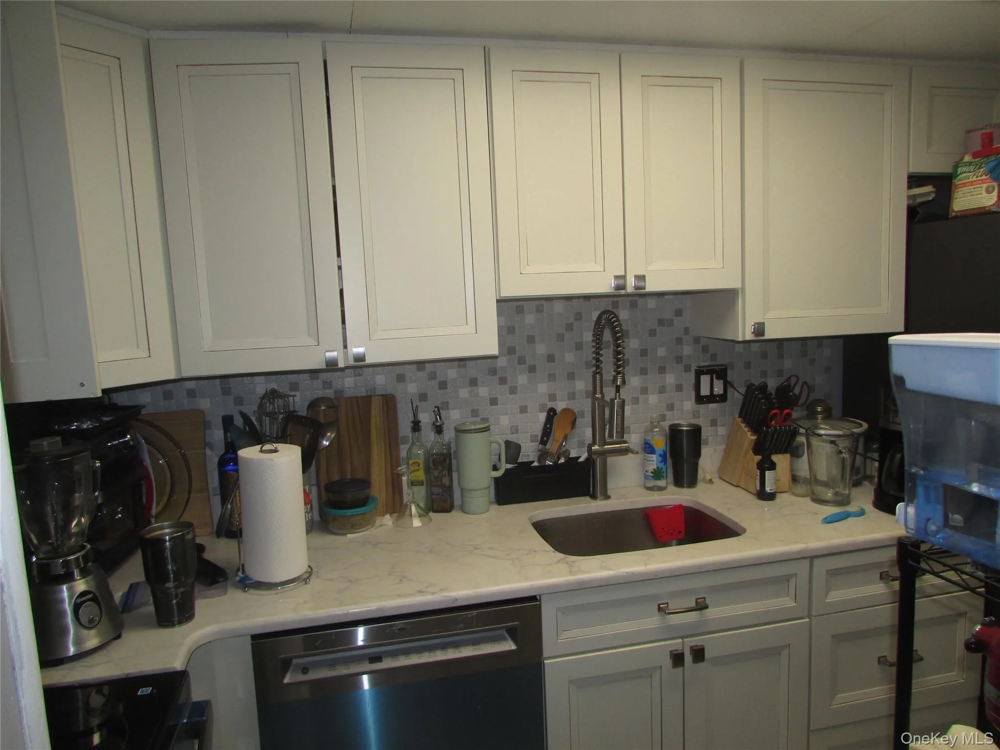 Kitchen featuring tasteful backsplash, dishwasher, and white cabinets Kitchen featuring tasteful backsplash, dishwasher, and white cabinets