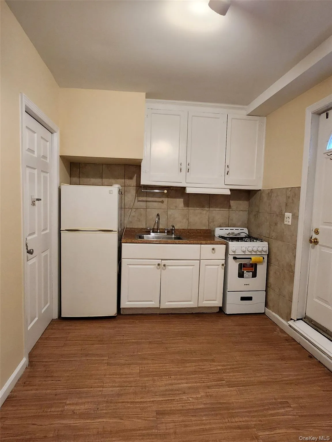 Kitchen featuring white cabinetry, dark countertops, white appliances, light wood-style flooring, and tile walls Kitchen featuring white cabinetry, dark countertops, white appliances, light wood-style flooring, and tile walls